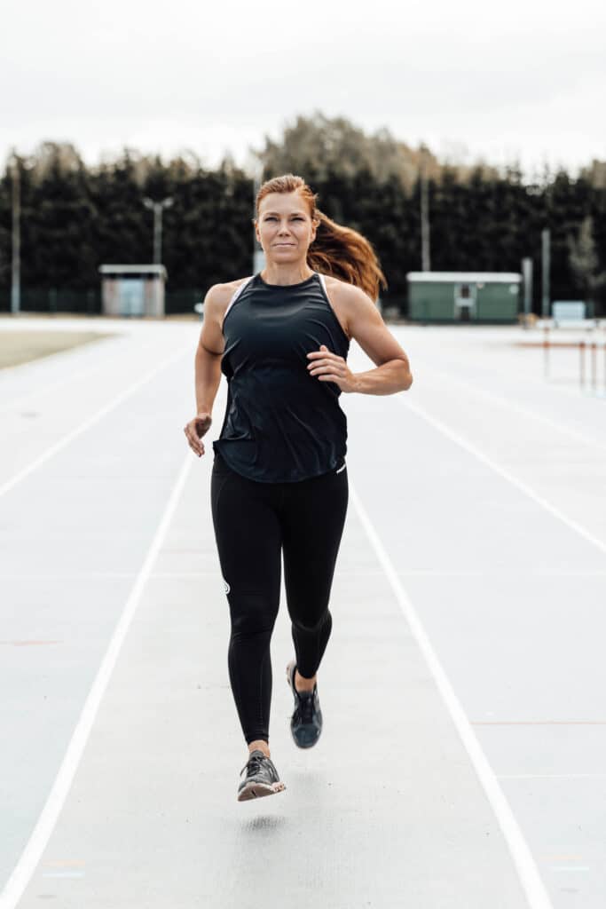 Hyvinvointi- ja juoksuvalmentaja Rebekka Jaakkola juoksee urheilukentällä.